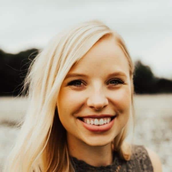 Smiling blonde woman outdoors by a lake, facing the camera.