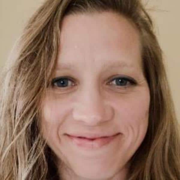 Close-up portrait of a smiling woman with long light brown hair, neutral background.
